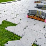 How to Protect Your Lawn While Entertaining Outdoors Stacked gray plastic floor tiles on grass, partially installed to create temporary protective walkways preventing lawn damage during events