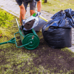 When to Topdress a Lawn A man pours dark topsoil from a plastic bag into a green wheeled topdresser.