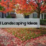 15 Fall Landscaping Ideas to Refresh Your Yard This Season A maple tree sheds leaves onto a green lawn in front of suburban homes.