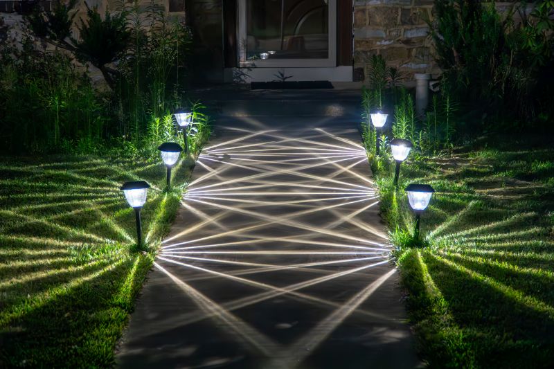 Six solar-style path lights line both sides of a concrete walkway at night, casting bright rays across the grass and path toward a lit front door.